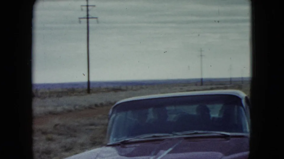 1960 Nevada roadside frame with the front of a red car at the edge of a sparse highway landscape.