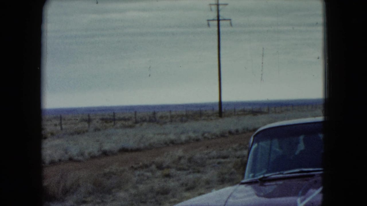 1960 Nevada 8mm frame showing part of a red car beside a flat roadside landscape with utility poles.