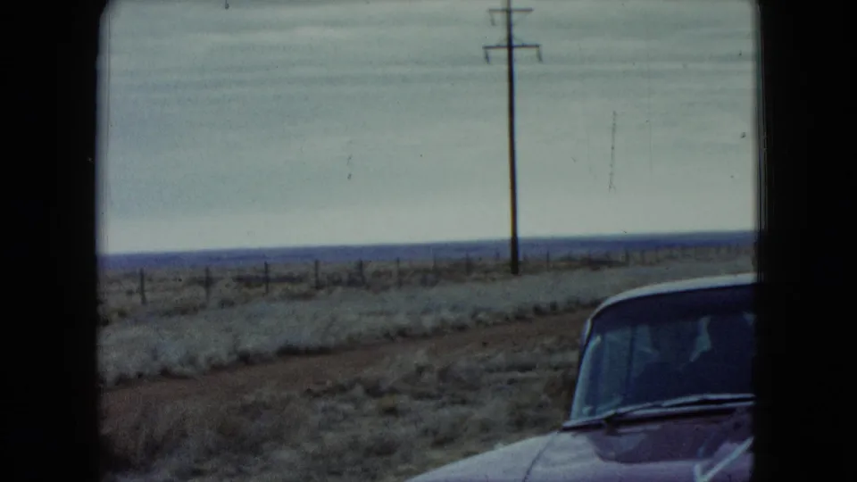 1960 Nevada 8mm frame showing part of a red car beside a flat roadside landscape with utility poles.