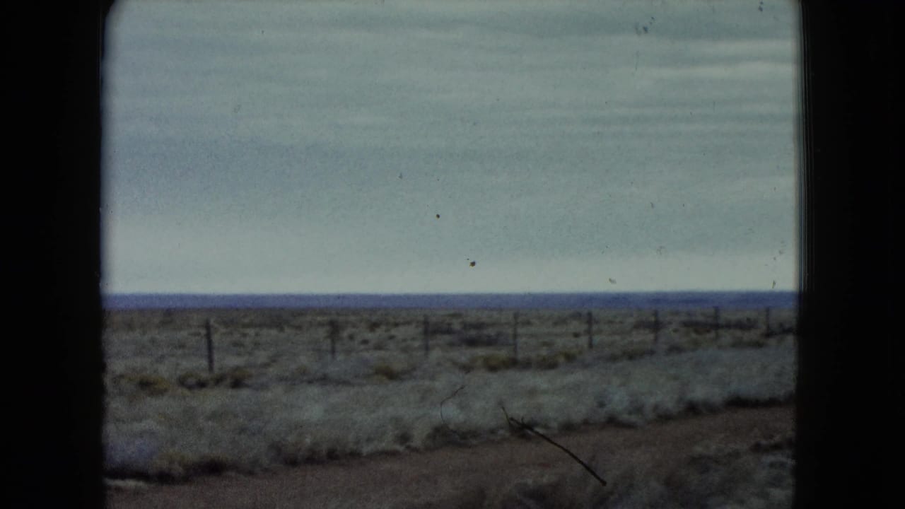 1960 Nevada highway-side view of scrubland, fence posts, and a wide horizon after the car leaves frame.