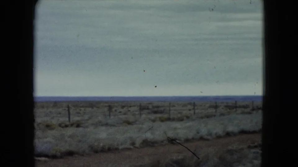 1960 Nevada highway-side view of scrubland, fence posts, and a wide horizon after the car leaves frame.