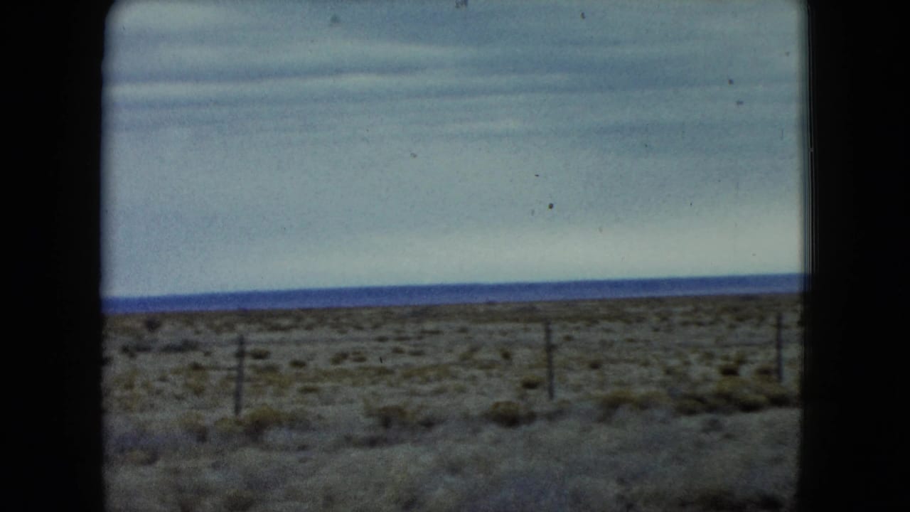 1960 Nevada 8mm frame showing fence posts, low scrub vegetation, and a broad cloudy sky over flat open land.