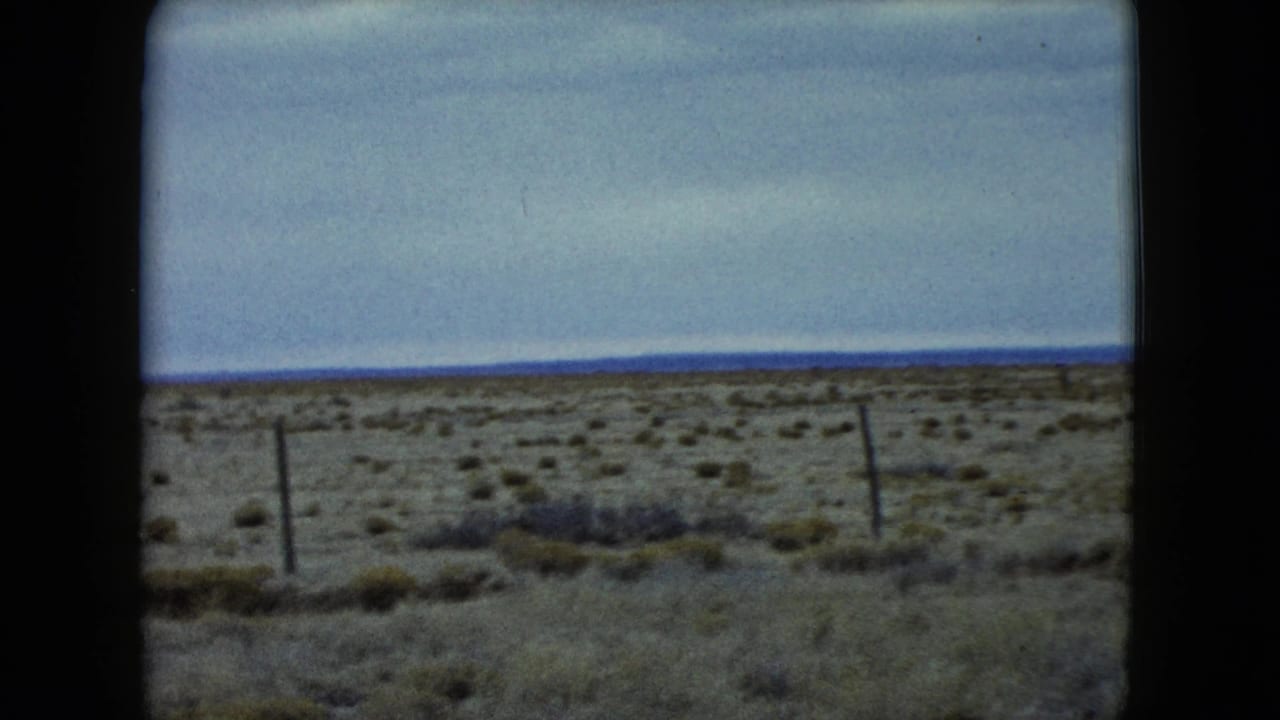 1960 Nevada frame showing arid scrubland, several fence posts, dry grass, and a distant horizon in soft 8mm color.