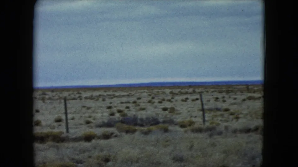 1960 Nevada frame showing arid scrubland, several fence posts, dry grass, and a distant horizon in soft 8mm color.