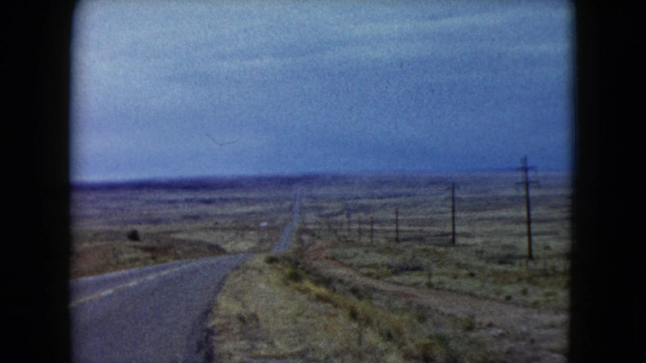 Empty desert highway receding toward the horizon under a cloudy sky.