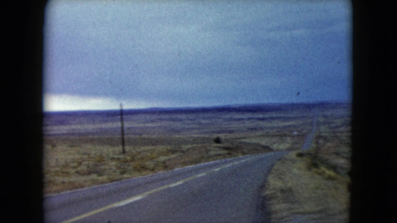 Two-lane road curving through open desert with utility poles beside it.