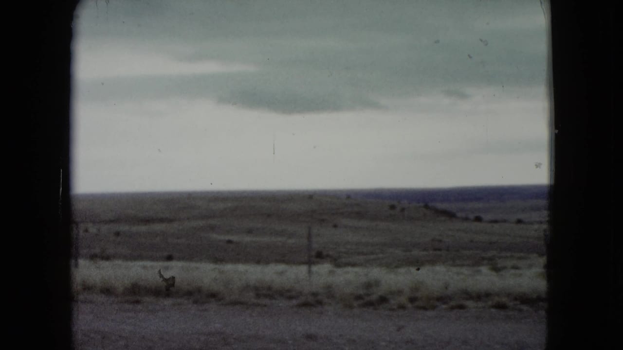 1960 8mm frame of an open Nevada desert plain with scrub, a distant horizon, and heavy film gate edges.