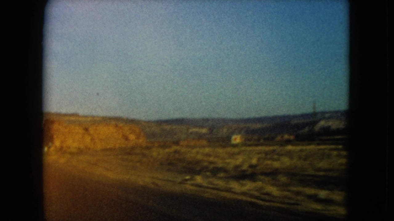 Blurred roadside desert with rocky hills and blue sky.