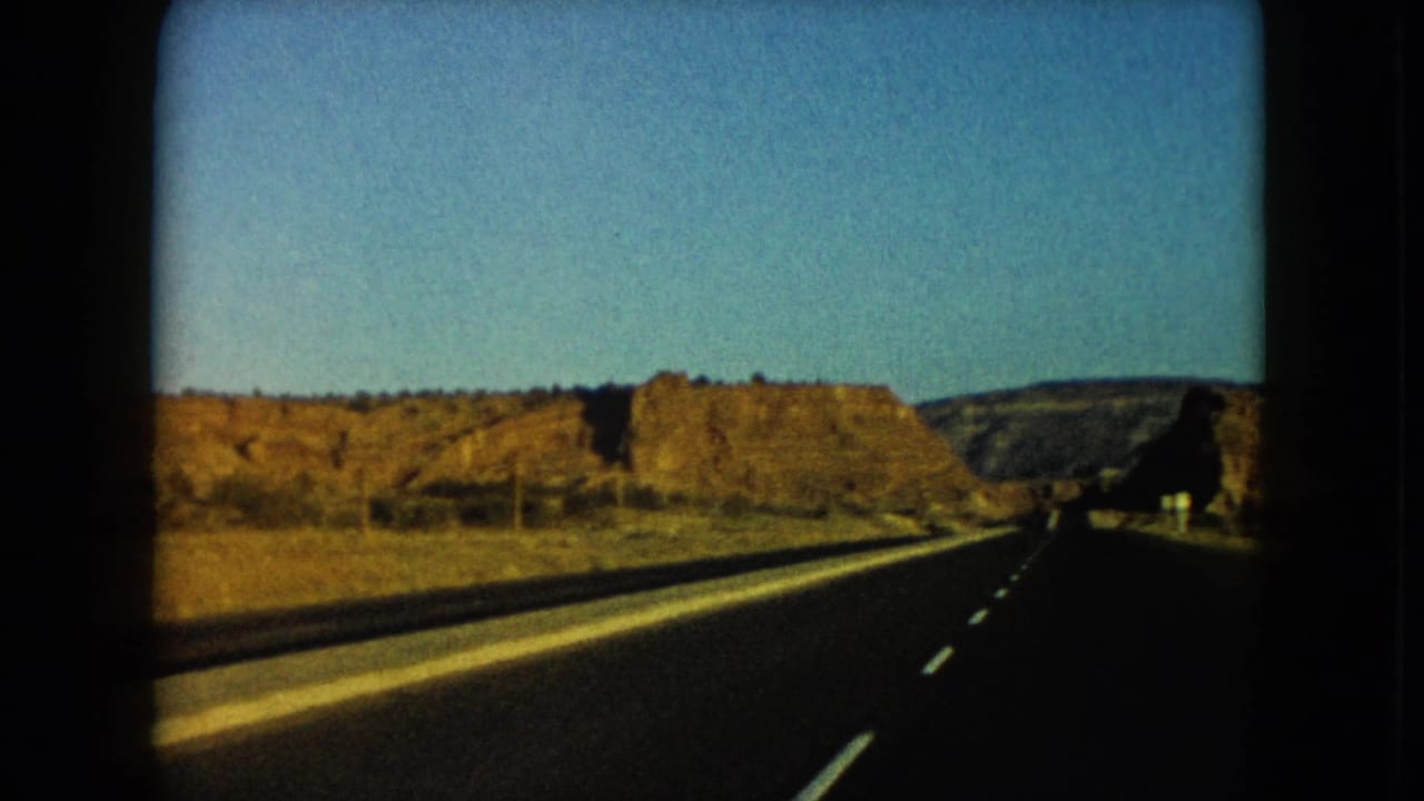 Two-lane highway running between golden desert hills under a blue sky.