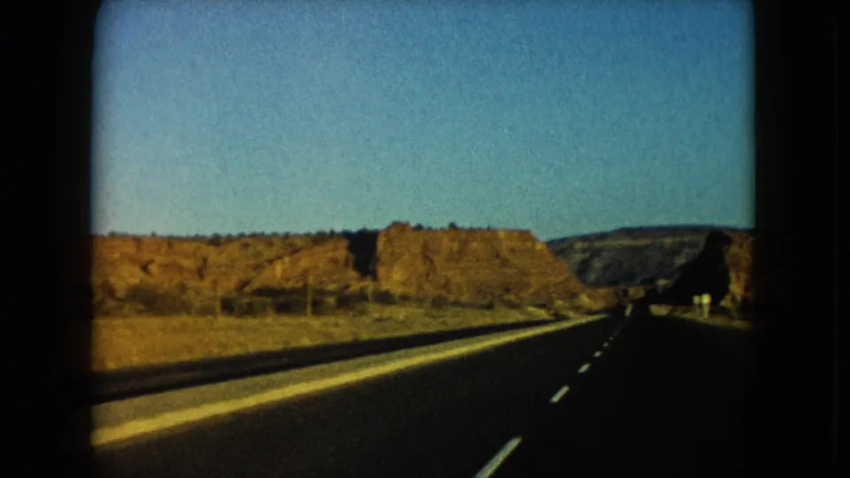 1960 Nevada 8mm view from a moving vehicle on a two-lane highway between rocky desert hills.