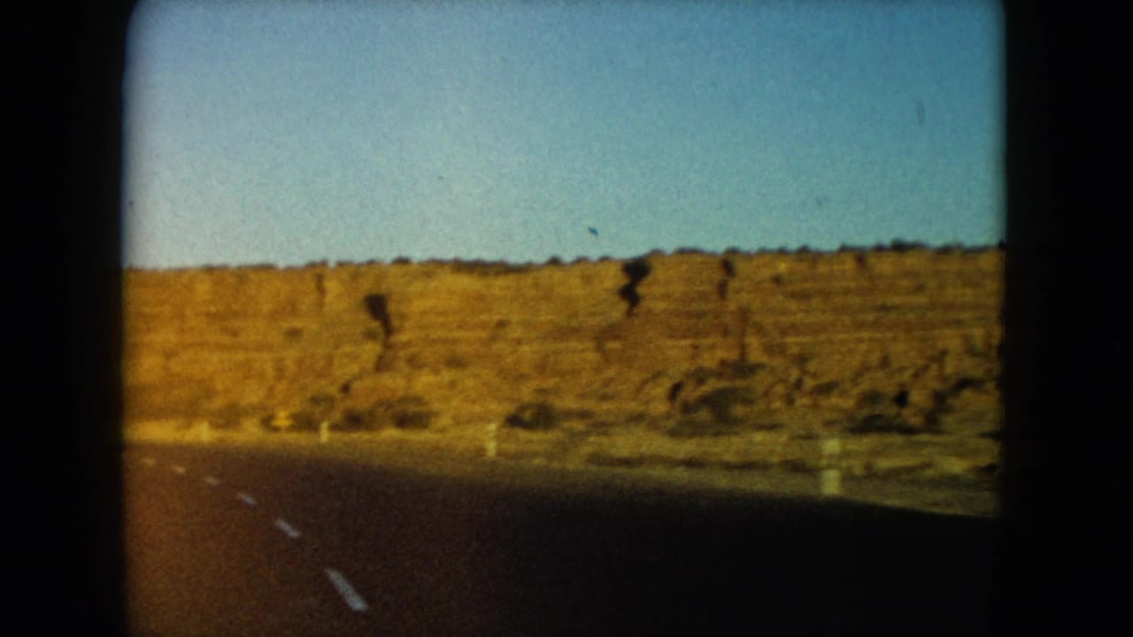 Curving desert highway beside a long golden rock wall and blue sky.