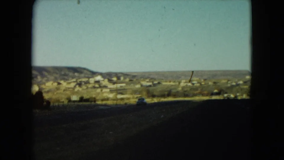 1960 Nevada roadside view of low buildings and hills beyond a shadowed highway foreground.