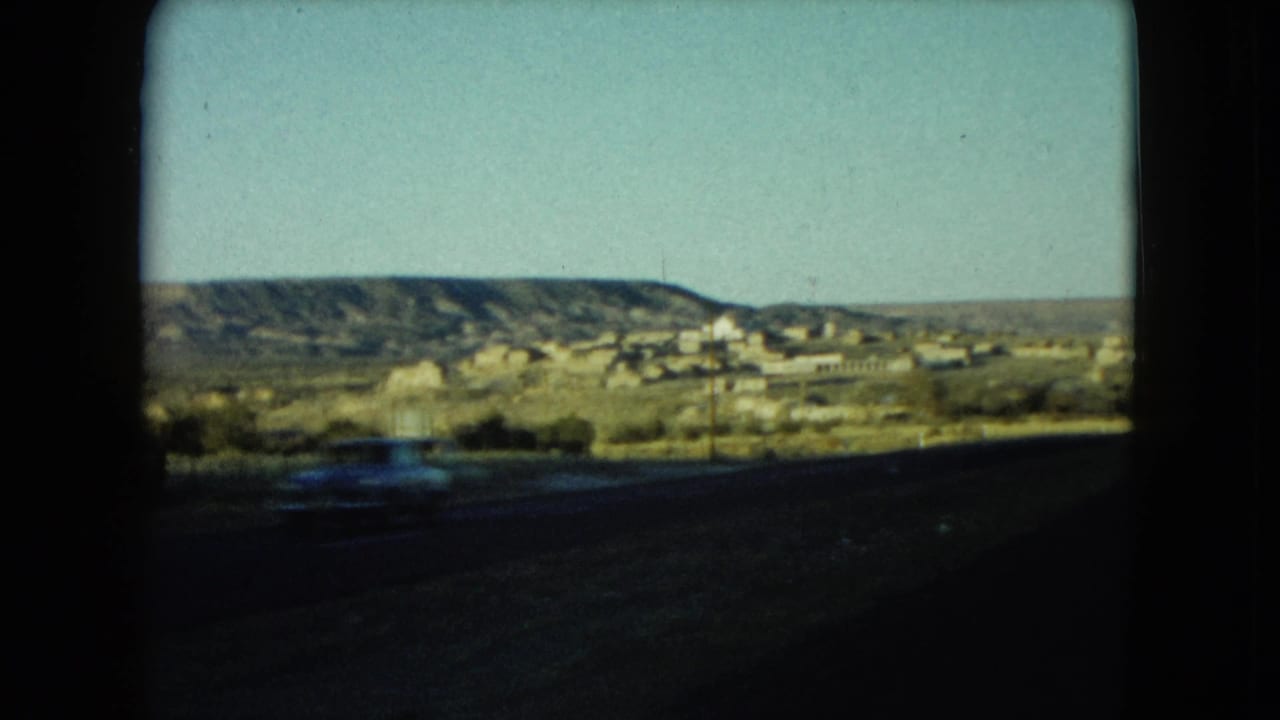 1960 Nevada 8mm roadside view with distant buildings, hills, utility poles, and a blurred car passing in front.