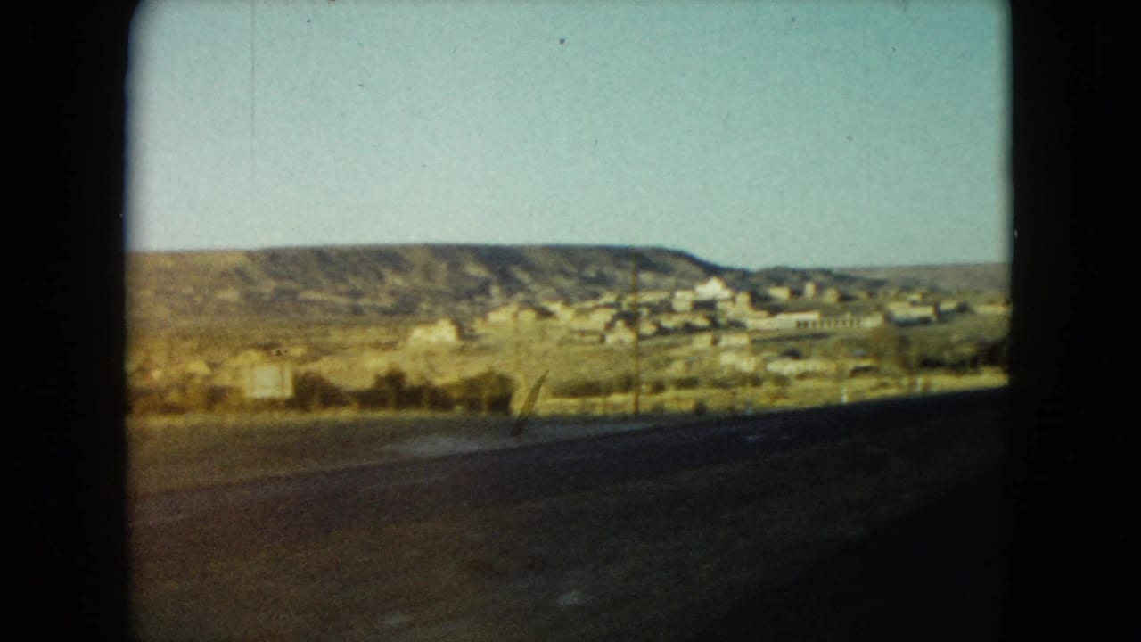 1960 Nevada 8mm frame showing a small town in the distance beyond arid hills and a dark roadside foreground.