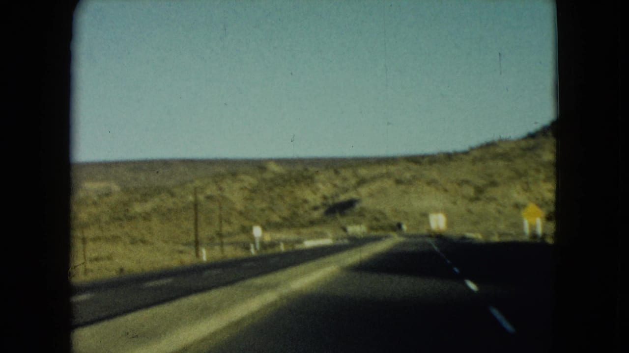 1960 Nevada road-travel frame showing an open two-lane highway through dry hills with utility poles and roadside signs.