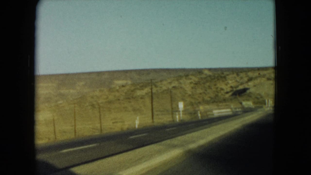 1960 Nevada road-trip view of a two-lane highway crossing dry hills, seen from a moving vehicle.