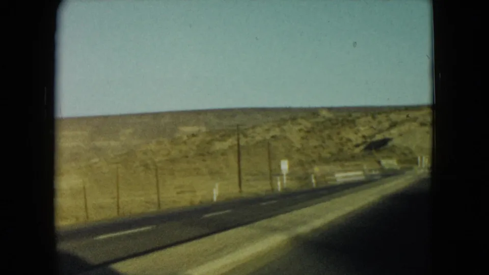 1960 Nevada road-trip view of a two-lane highway crossing dry hills, seen from a moving vehicle.