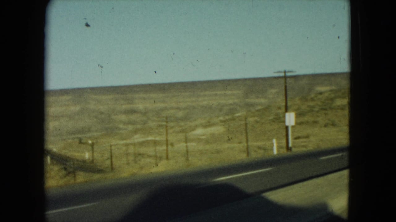 Roadside curve through dry open terrain with utility poles and a small sign.