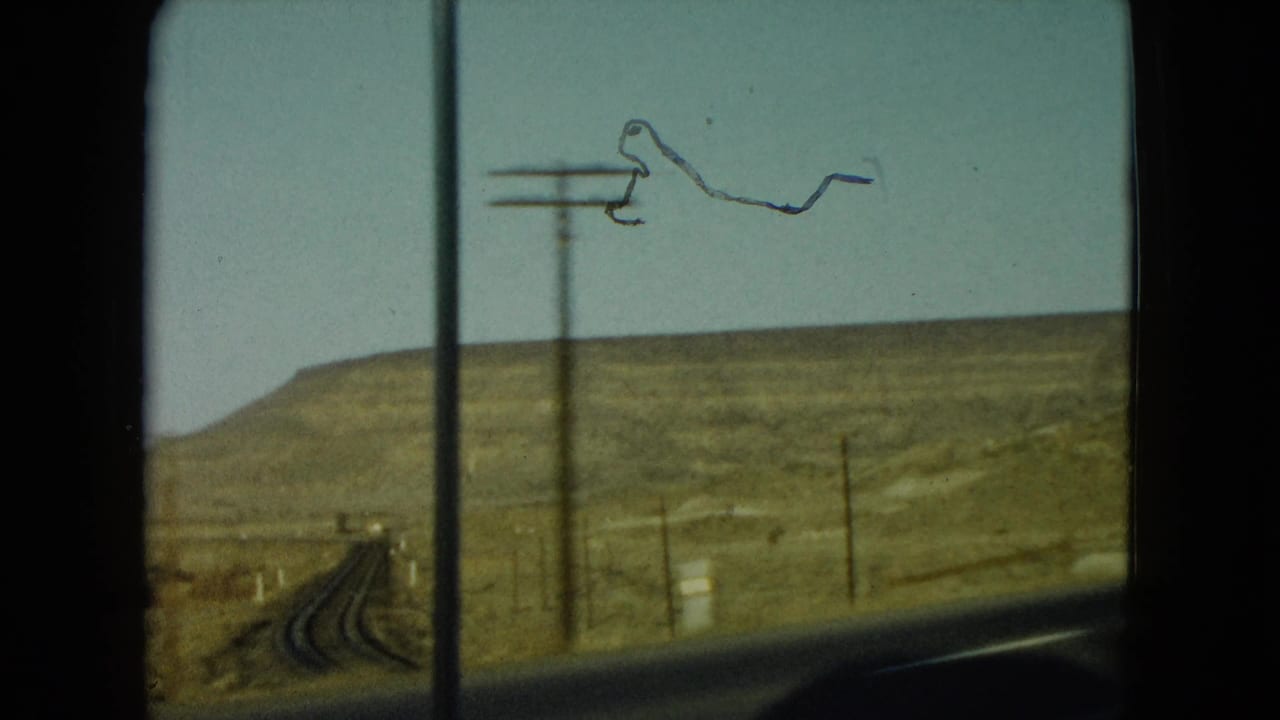 1960 Nevada home-movie frame showing a desert roadway, utility poles, and open hills from inside a moving car.