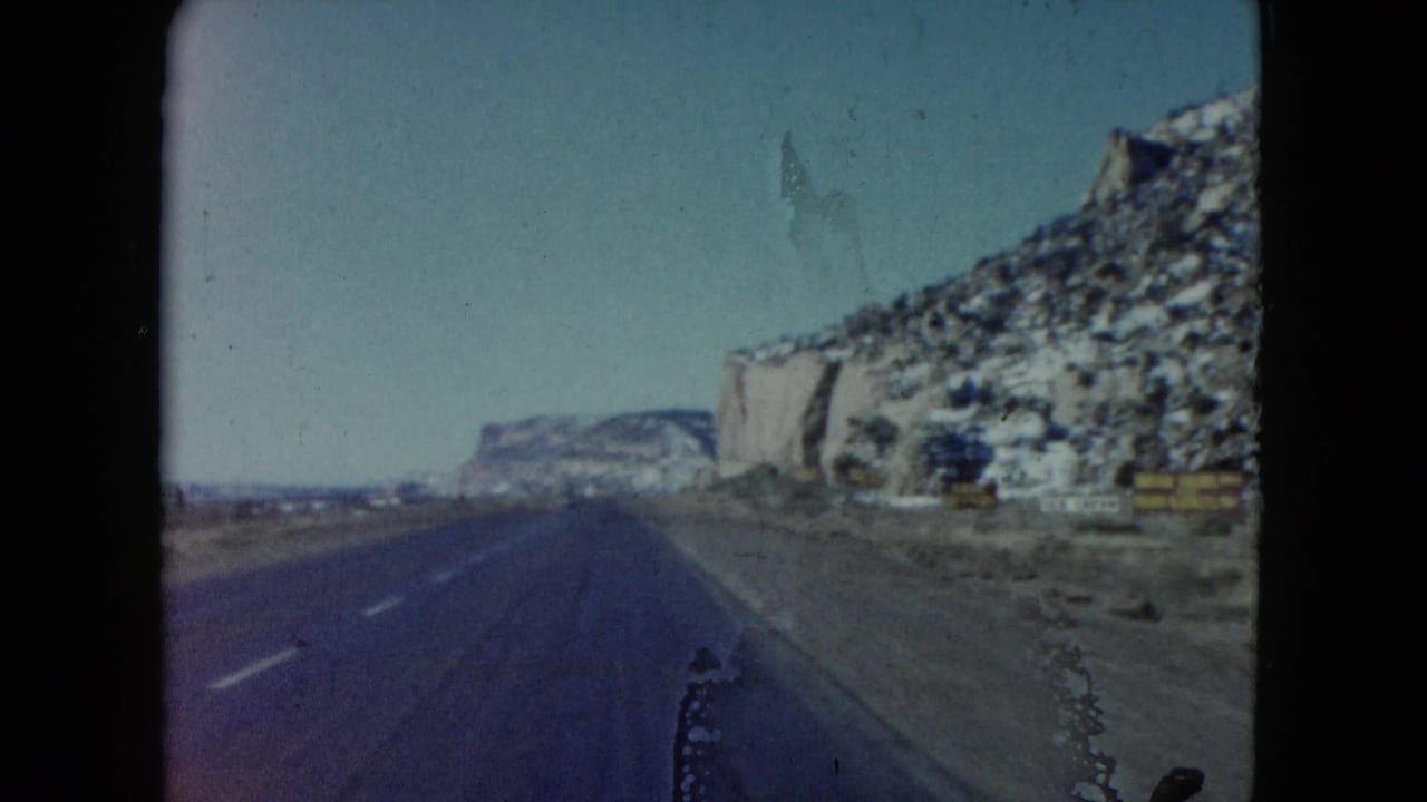 1960 Nevada 8mm road view showing a paved highway, shoulder, distant mesa, and pale rock formations.