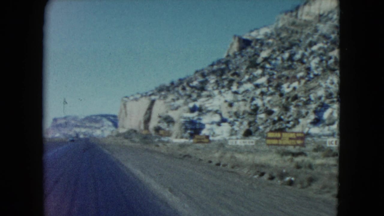 Desert highway curving past rocky hillsides and roadside signs.