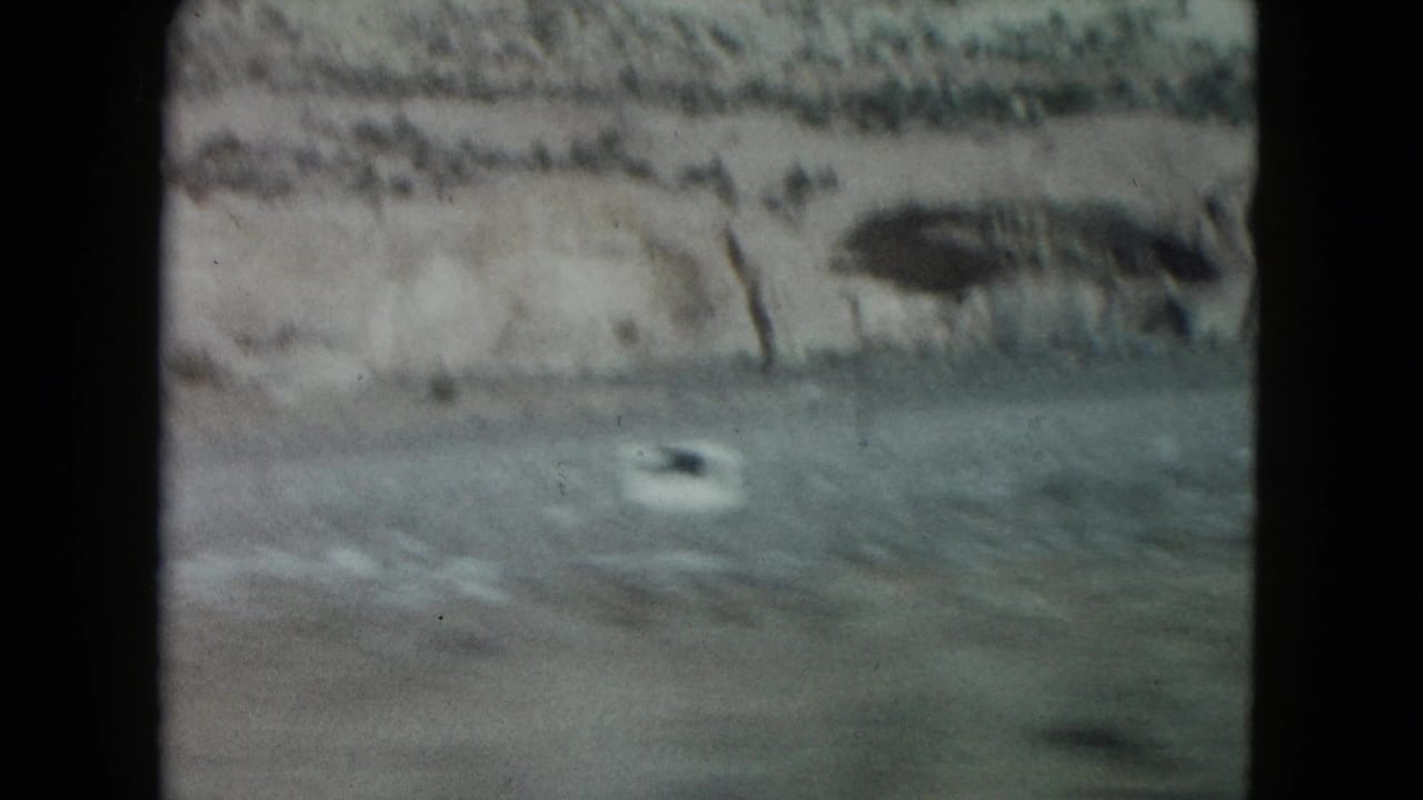 1960 Nevada home-movie frame showing a blurred roadside and pale rocky cliffs filmed from a moving vehicle.