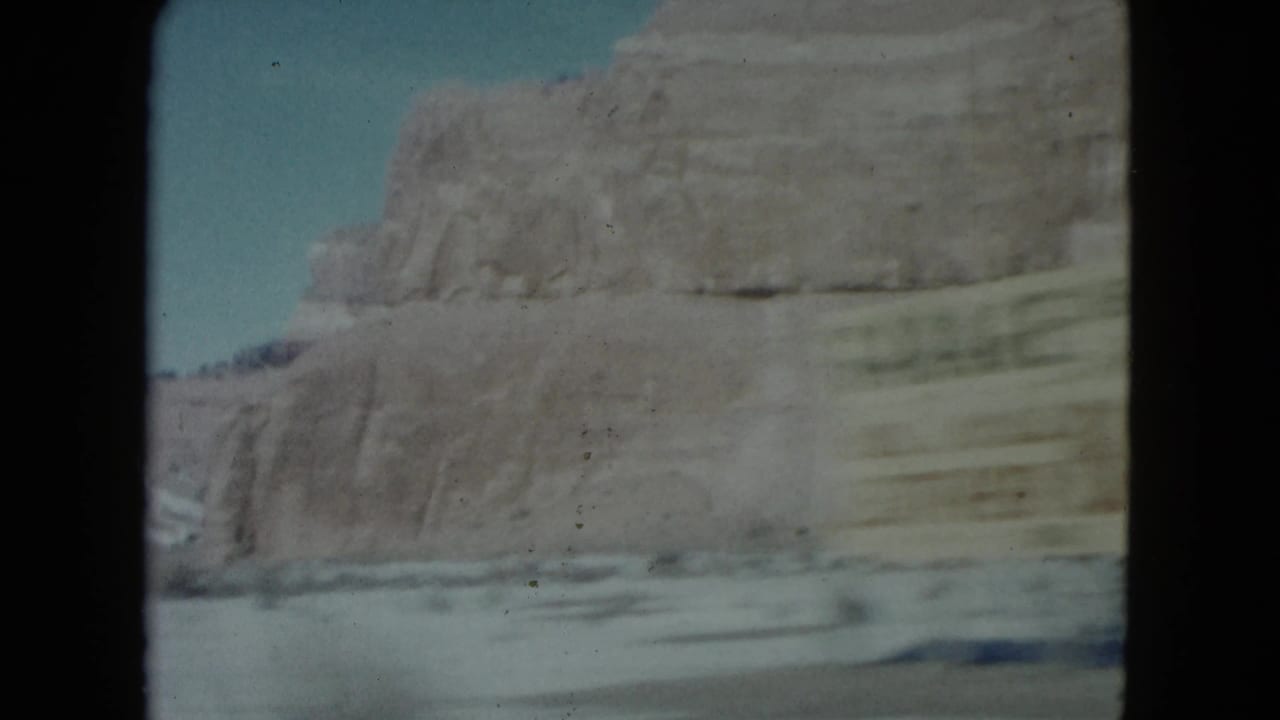 Desert rock formation and blurred roadside ground viewed from a moving vehicle.