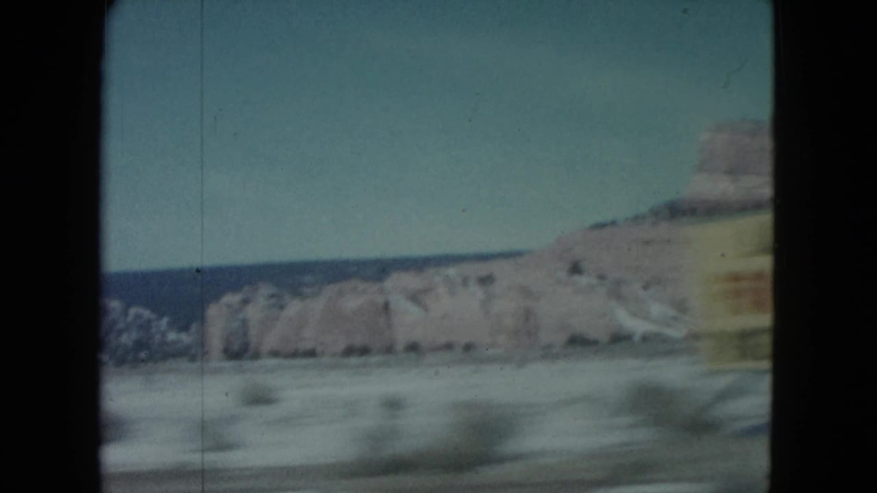 Roadside desert landscape with mesas and a partly visible yellow sign.