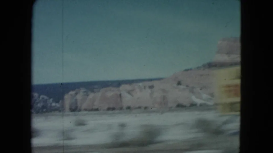 Nevada desert road view with distant rock formations and a briefly visible yellow roadside sign.