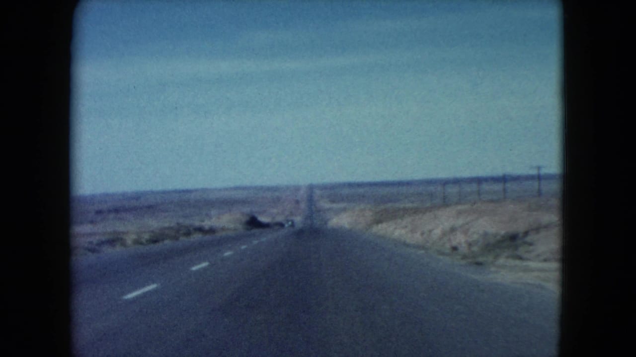 Vehicle-shot 8mm frame of a desert highway with utility poles and scrubland, consistent with the listed 1960 Southwest trip.