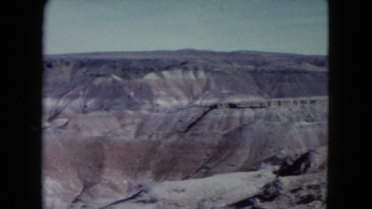 1960 Nevada 8mm frame showing eroded desert ridges, mesas, and muted rock layers beneath a pale sky.