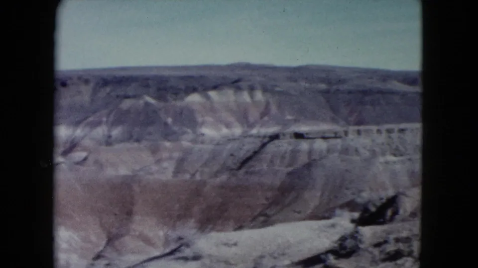 1960 Nevada 8mm frame showing eroded desert ridges, mesas, and muted rock layers beneath a pale sky.