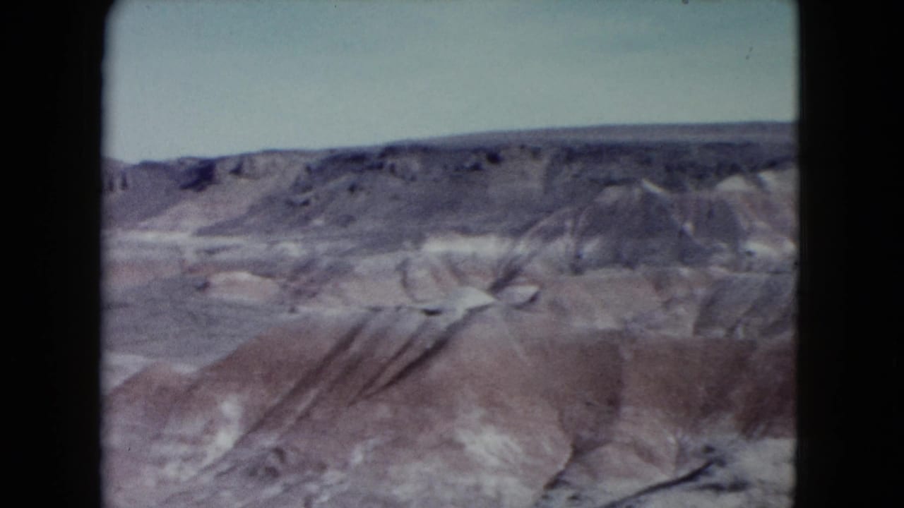 1960 Nevada home-movie frame with a wide view of mesa edges, dry gullies, and open desert terrain.