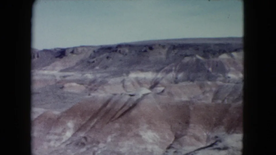 1960 Nevada home-movie frame with a wide view of mesa edges, dry gullies, and open desert terrain.