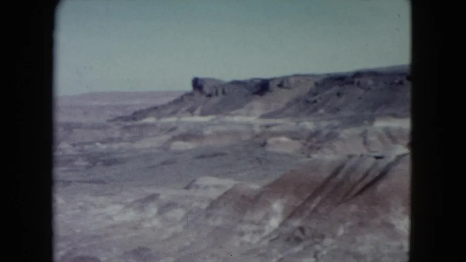 1960 Nevada 8mm frame showing an open desert basin, flat-topped ridge, and softly rendered eroded foreground.