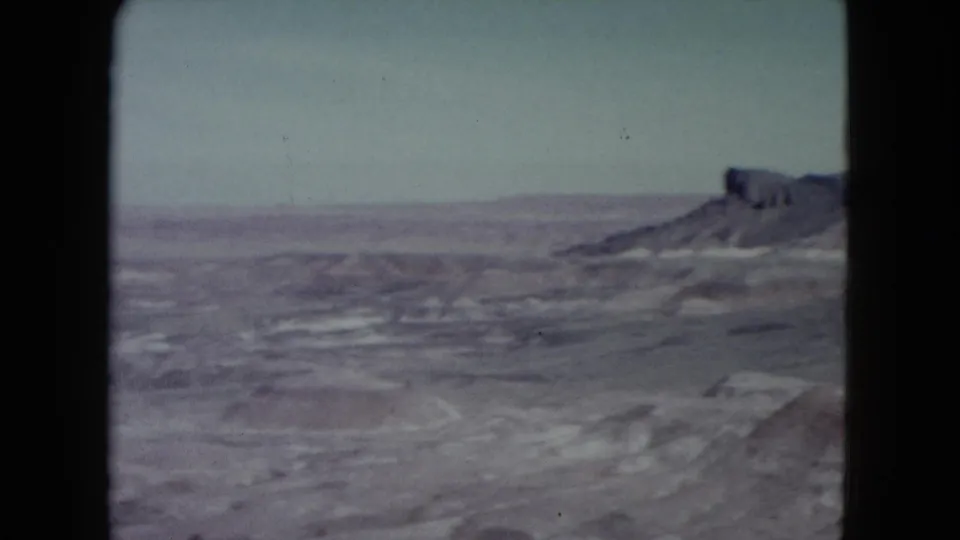 1960 Nevada home-movie frame looking over a dry plain toward distant mesas and low eroded hills.