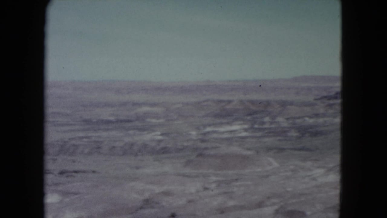 Wide rocky desert landscape beneath a pale sky with distant low mountains.