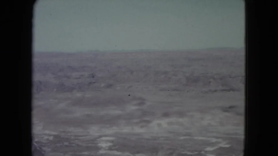 1960 8mm view of open Nevada desert terrain, distant low ridges, and a washed-out sky framed by black film edges.