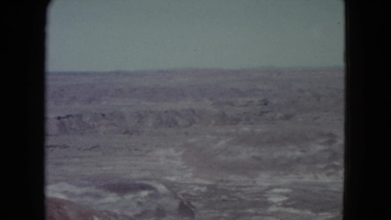 Faded 1960 Nevada home-movie frame showing barren desert flats, low ridgelines, and a pale overcast sky.
