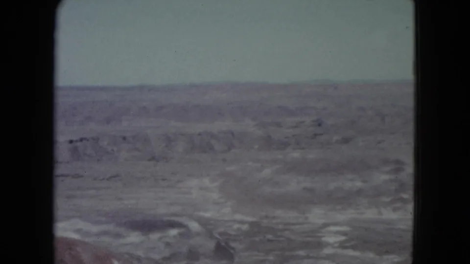 Faded 1960 Nevada home-movie frame showing barren desert flats, low ridgelines, and a pale overcast sky.