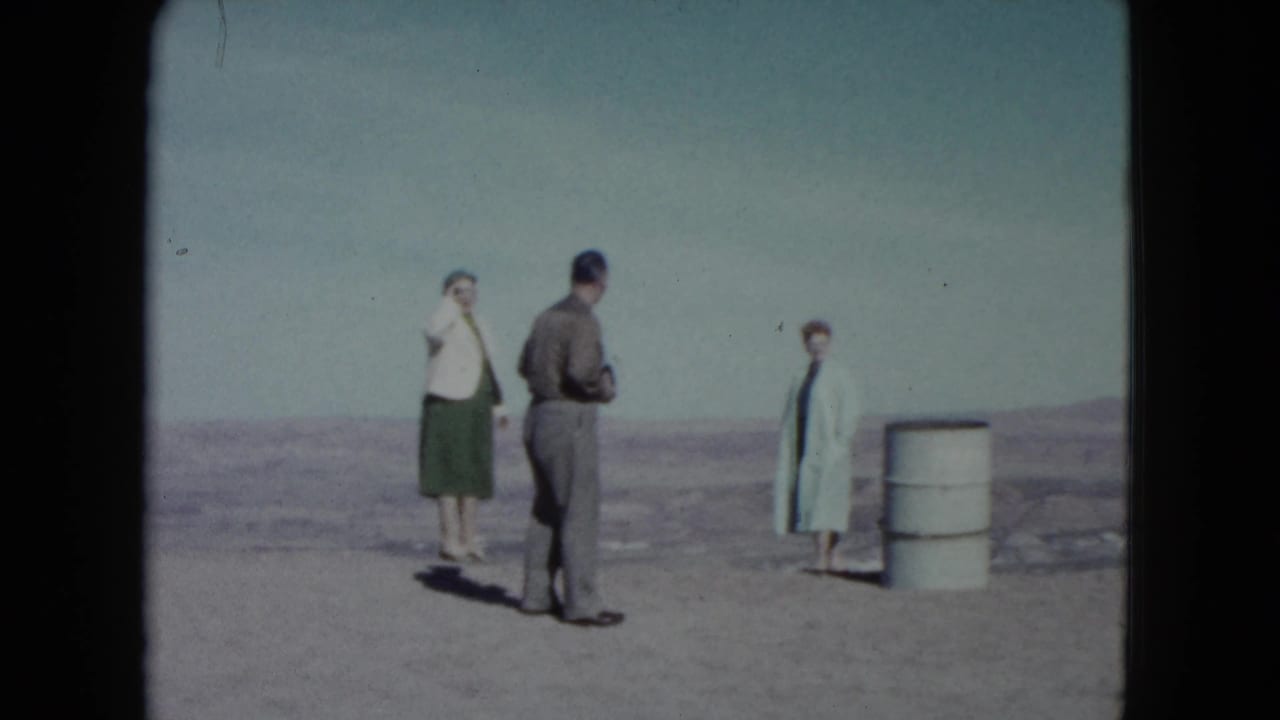 Three adults stand in a Nevada desert landscape beside a white barrel.