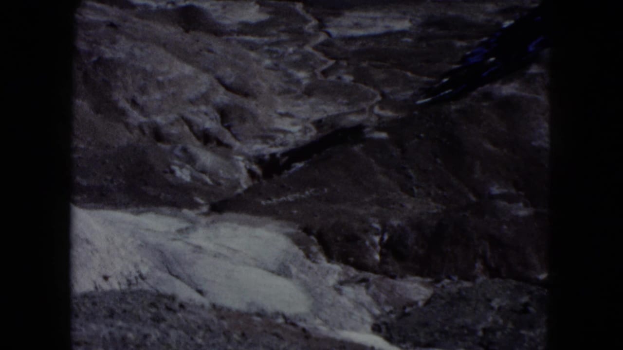 1960 Nevada 8mm frame with eroded desert ridges, pale flats, and dark film borders from a visitor-shot canyon view.