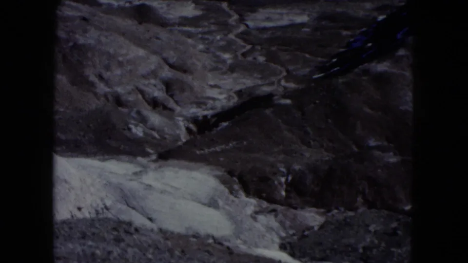 1960 Nevada 8mm frame with eroded desert ridges, pale flats, and dark film borders from a visitor-shot canyon view.