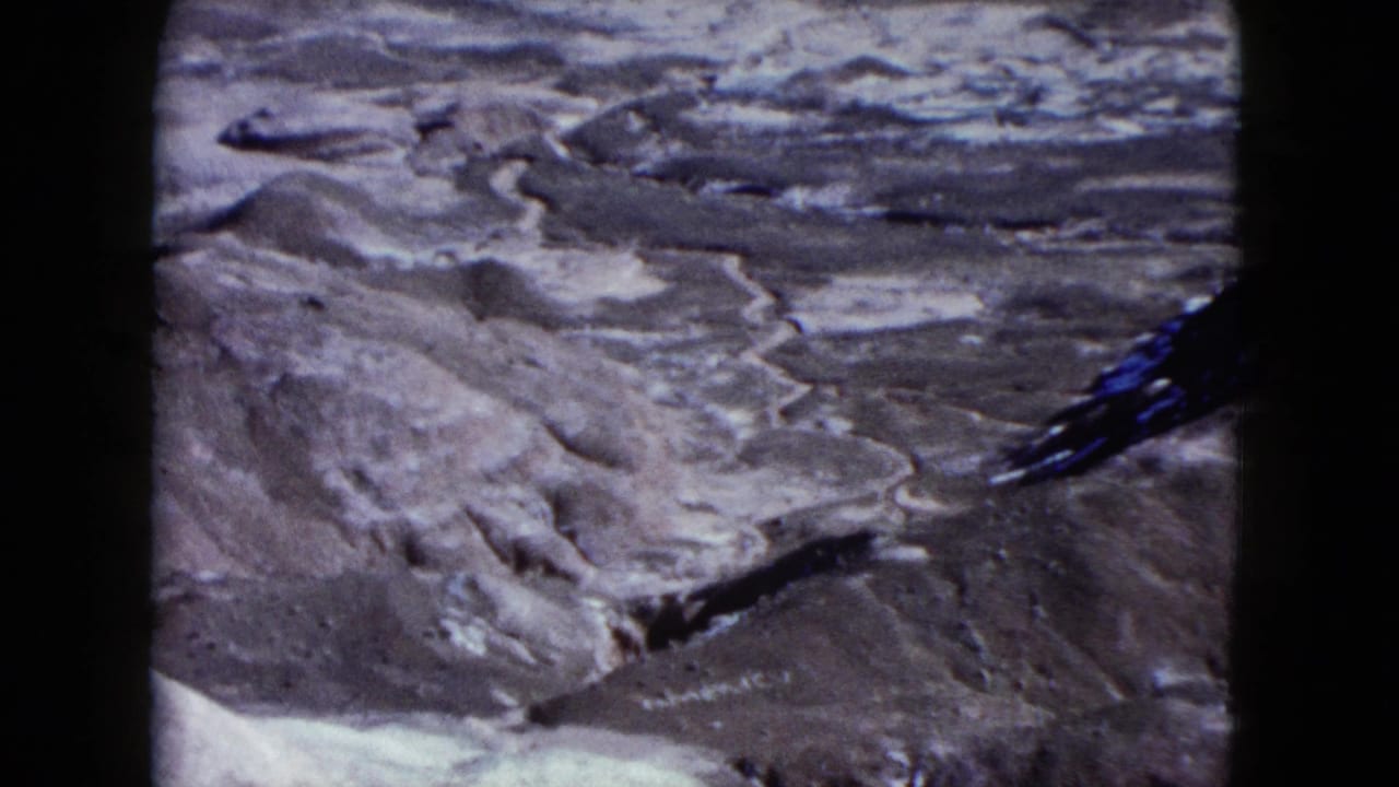 A 1960 Nevada home-movie view appears to look down across pale eroded canyon channels and rocky desert ground.