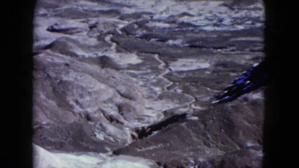 A 1960 Nevada home-movie view appears to look down across pale eroded canyon channels and rocky desert ground.