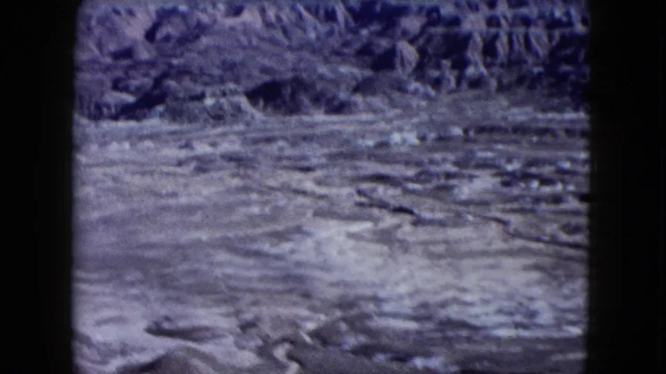 A wide 8mm Nevada desert view shows flat arid ground below darker ridges, with soft focus and visible film grain.