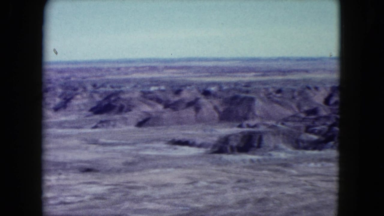 Wide desert overlook with pale sky, eroded ridges, and dark 8mm frame borders.