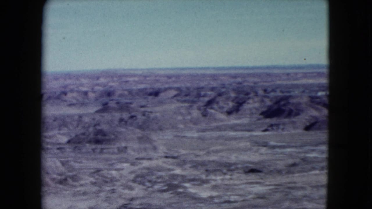 1960 Nevada home-movie frame showing broad desert flats and low eroded hills from an overlook.