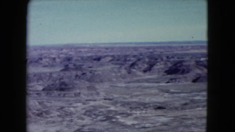 1960 Nevada home-movie frame showing broad desert flats and low eroded hills from an overlook.