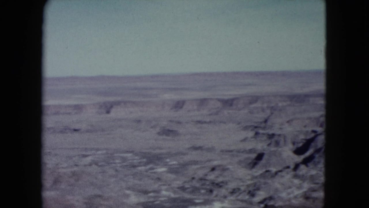 1960 Nevada 8mm frame showing distant eroded desert ridges and dry terrain under a pale sky.